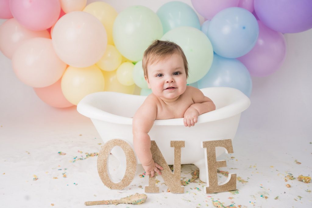 Rainbow balloons in background with baby in a bathtub